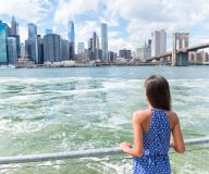 Kvinna vid vattnet med utsikt över New Yorks skyline och Brooklyn Bridge.