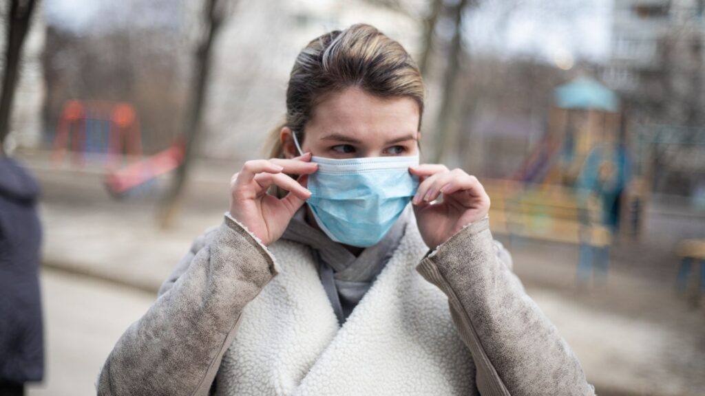 Kvinna sätter på sig en blå mask utomhus i en lekpark.