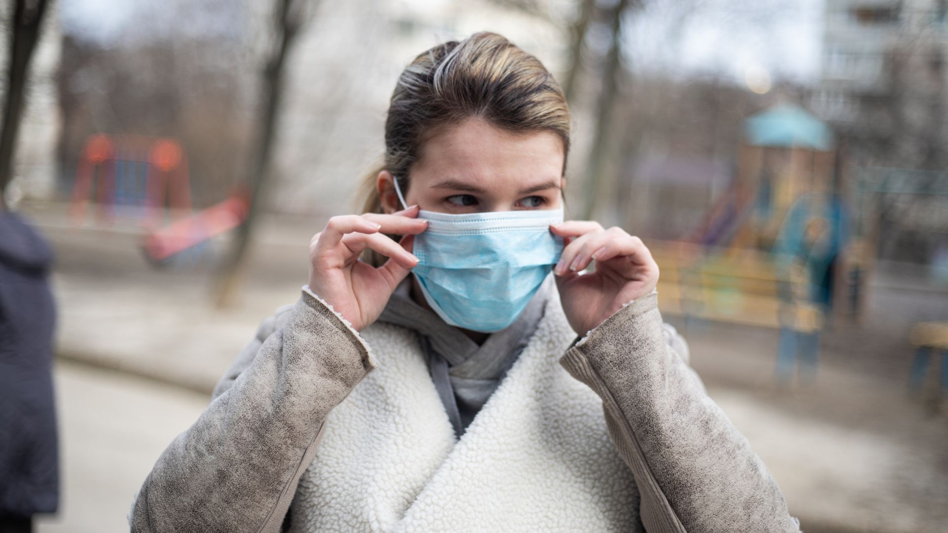 Kvinna sätter på sig en blå mask utomhus i en lekpark.